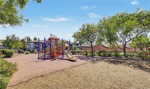 Ein Spielplatz mit Rutsche und Klettergerüsten, umgeben von Bäumen und Wohnhäusern.