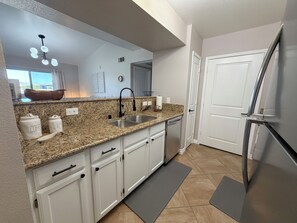 Eine moderne Küche mit Granit-Arbeitsplatten, weißen Schränken, einer Edelstahl-Spüle und einem Kühlschrank.
