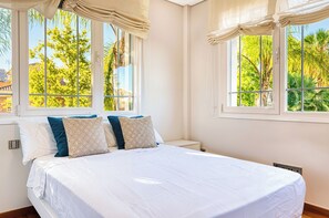Un dormitorio con cama, dos ventanas y vistas a árboles.