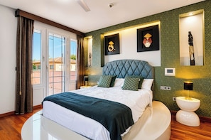 Un dormitorio con una cama, una mesa redonda, una mesita de noche y vistas al exterior.