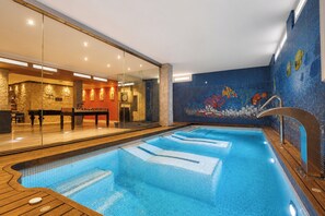 Una piscina con cubierta de madera, pared de vidrio y un mural de peces.