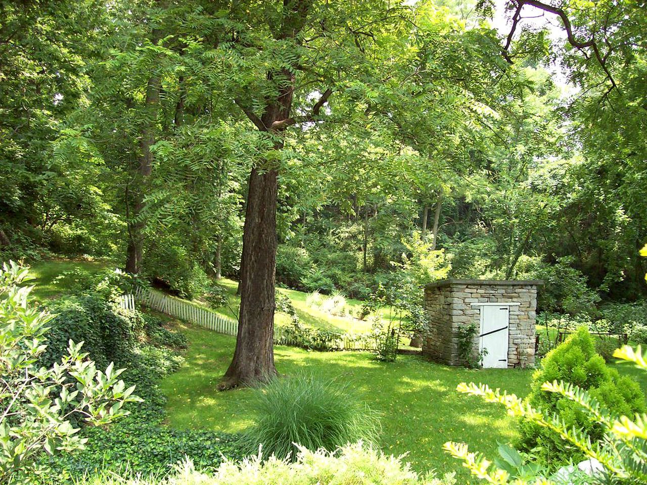 Un jardín exuberante con un árbol grande, una estructura de piedra y una cerca de madera.