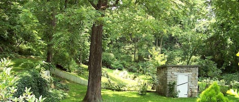 Un jardín exuberante con un árbol grande, una estructura de piedra y una cerca de madera.