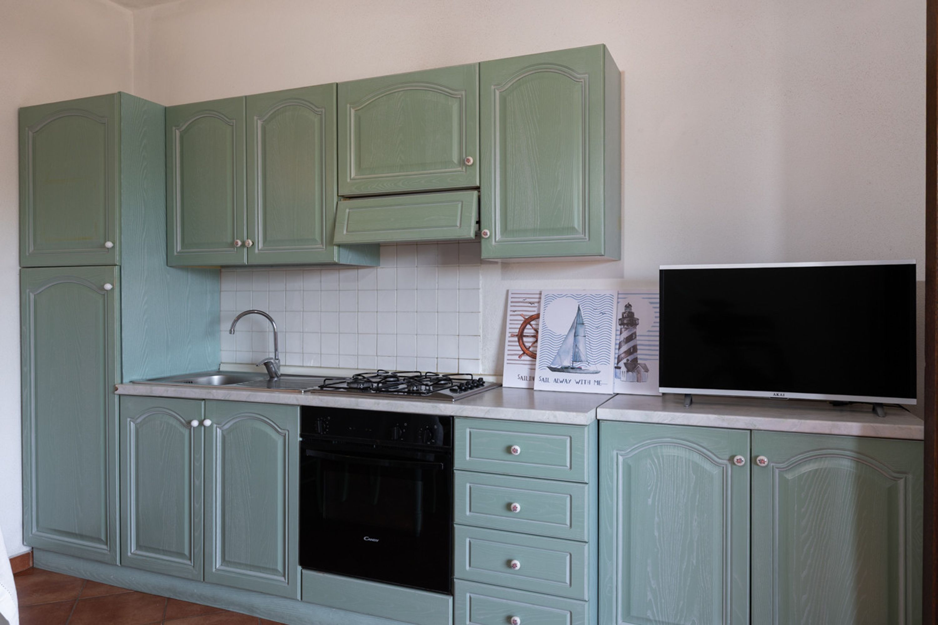 A kitchen with green cabinets, a stove, a sink, and a television.
