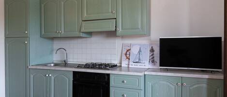 A kitchen with green cabinets, a stove, a sink, and a television.