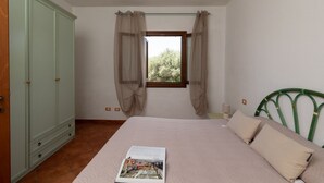 Une chambre à coucher avec un lit, une fenêtre avec des rideaux, une armoire et une table de chevet.