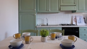 Une cuisine avec des meubles de couleur verte, un plan de travail blanc et une table à manger mise avec des bols, des tasses et une plante en pot.