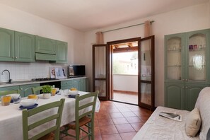 A kitchen with green cabinets, a dining table with chairs, a TV, and a sliding glass door leading to an outdoor area. - Casa Dell Edera F2 1 by Wonderful Italy (San Teodoro)