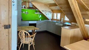 A kitchen with a green countertop, wooden cabinets, a wooden dining table, and a chair. - Chasa Soldanella, (Tarasp) by Interhome (Tarasp)