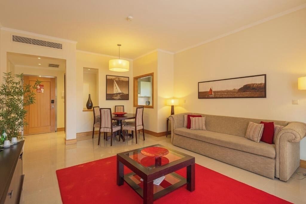 A living room with a sofa, a coffee table, a dining table with chairs, and a painting on the wall.