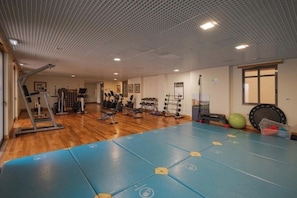 Een fitnessruimte met trainingsapparatuur, een blauw matgedeelte en een houten vloer.