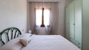 Un dormitorio con cama, armario y ventana con cortinas.