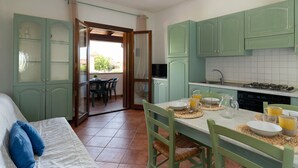 Una habitación con una cama, una mesa de comedor preparada para dos personas y una zona de cocina con armarios verdes y un salpicadero de azulejos.