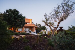 Un edificio de dos pisos con piscina, rodeado de árboles y plantas.