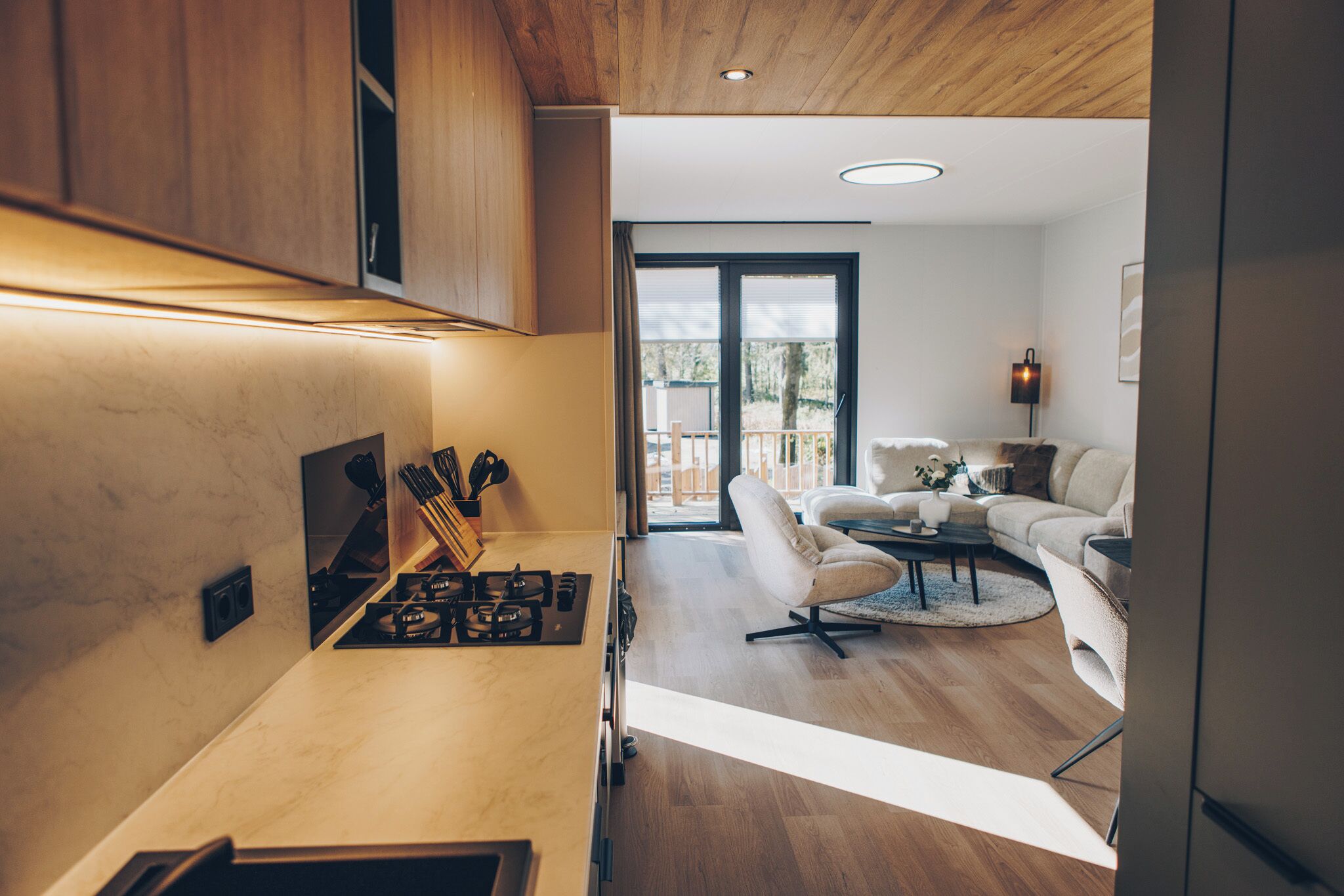 Een moderne keuken met een gasfornuis, houten kasten en een zithoek met een witte bank en een salontafel.