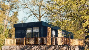 A modern cabin with a balcony, surrounded by trees.