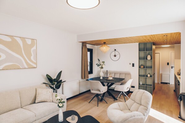 Un salon moderne avec un canapé, des fauteuils, une table à manger et un coin cuisine à l’arrière-plan.