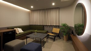 Una sala moderna con sofá, mesa de centro, sillón, mesita, planta en maceta, espejo y lavavajillas.