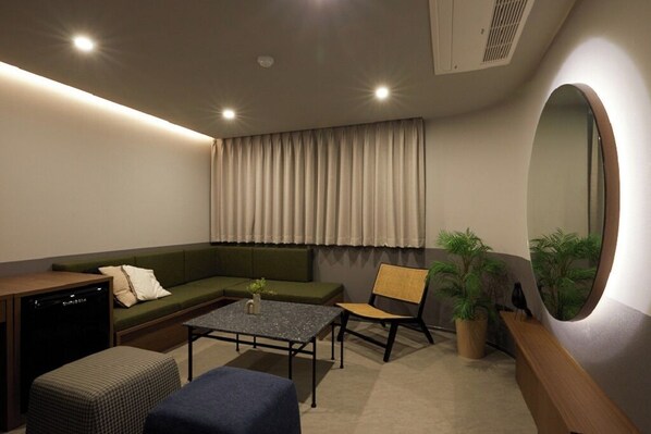 Una sala moderna con sofá, mesa de centro, sillón, mesita, planta en maceta, espejo y lavavajillas.