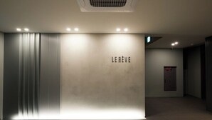 Una zona de recepción moderna con un cartel 'LE RÉVE', un panel vertical y una puerta con un botón de emergencia rojo.