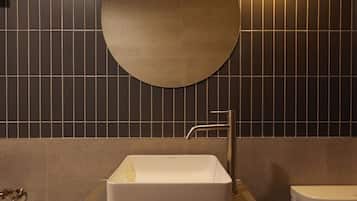A bathroom with a round mirror, a rectangular sink, a toilet, and a towel dispenser.
