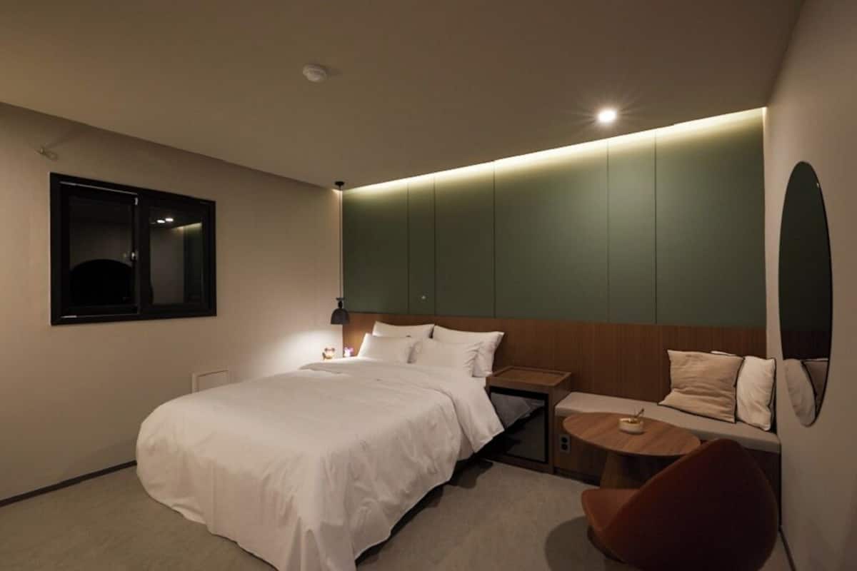 Quarto de hotel moderno com uma cama grande, uma mesa pequena, uma cadeira e uma mesinha de cabeceira.