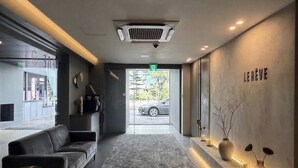 A modern lobby with a grey carpet, a sofa, a small table, and a reception desk with a sign that reads 'LE HEUVE'. - Lereve Hotel (Seoul)