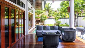 Un espacio al aire libre techado con piscina, mobiliario de mimbre y ventilador de techo.
