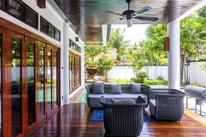 Un espacio al aire libre techado con piscina, mobiliario de mimbre y ventilador de techo.