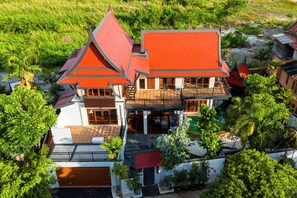Un edificio grande de varios pisos con techo rojo, múltiples balcones y rodeado de abundante vegetación.