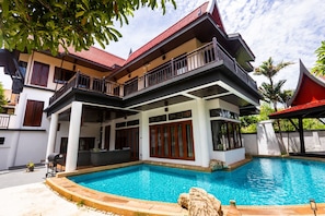 Ein zweistöckiges Haus mit Swimmingpool, Balkon und rotem Dach.