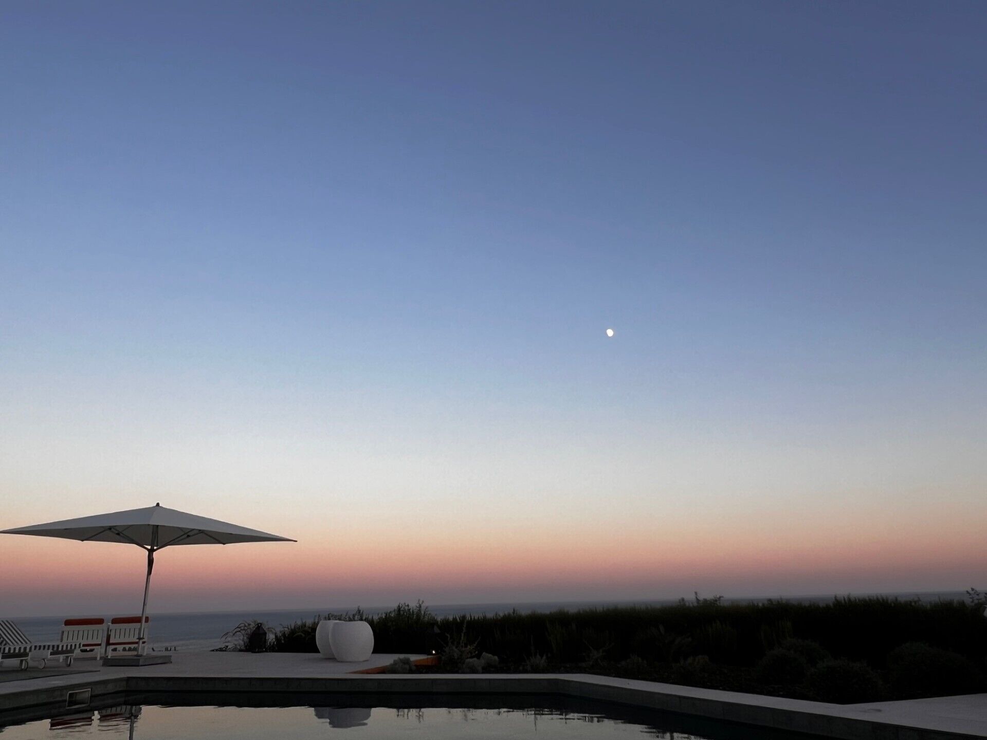 Una piscina con sillones de descanso y una sombrilla, con vistas a un cuerpo de agua y un cielo despejado.