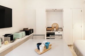 Una habitación moderna y minimalista con una televisión de pantalla plana, una mesa con tazas, un tostador y un armario blanco.