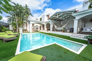 Ein Pool mit grünen Liegestühlen, einer Hängematte und einer überdachten Terrasse.