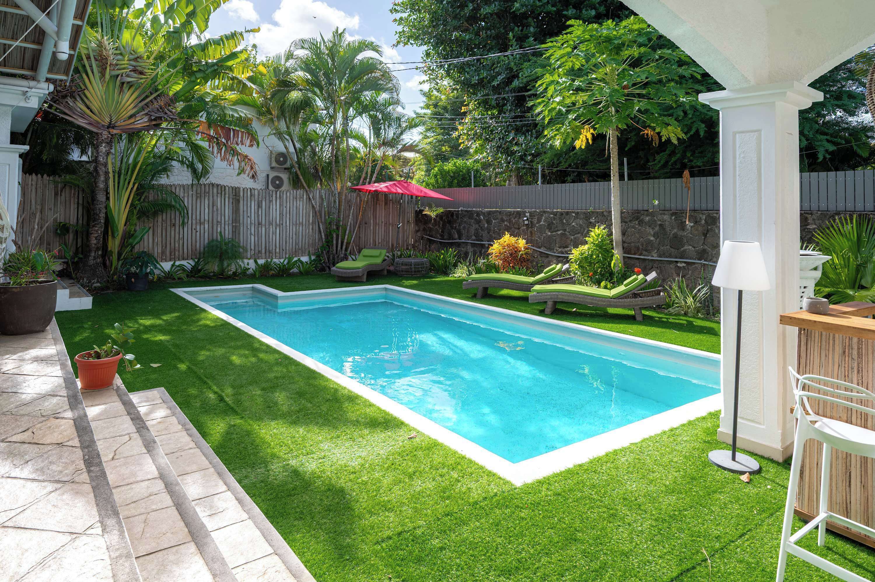 Ein Pool mit Kunstgrashallett, einer Holzterrasse und einer Steinmauer.