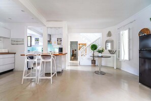 Eine moderne Küche mit weißen Schränken, einem Essbereich mit weißen Stühlen, einem schwarzen Kühlschrank und einer Treppe zu einer weiteren Ebene.