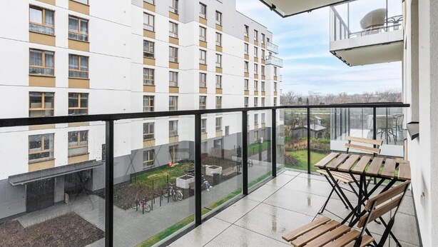 Ein Balkon mit Blick auf ein mehrstöckiges Gebäude, einer Glasreling und Gartenmöbeln.