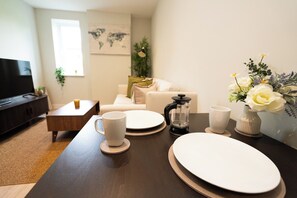 Ein modernes Wohnzimmer mit einem dunkelholznen Couchtisch, weißen Tellern, Tassen und einer Blumenkomposition.