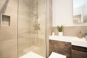 Ein modernes Badezimmer mit einer einteiligen Duschkabine, einem weißen Waschbecken, einem Spiegel und einer Topfpflanze.