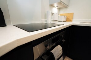 Eine Küche mit einem schwarzen Induktionskochfeld, einer weißen Arbeitsplatte, einem Holzschneidebrett und einem weißen Toaster.