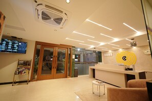 Un área de recepción moderna con entrada por puerta de vidrio, mostrador de recepción y un reloj montado en la pared.