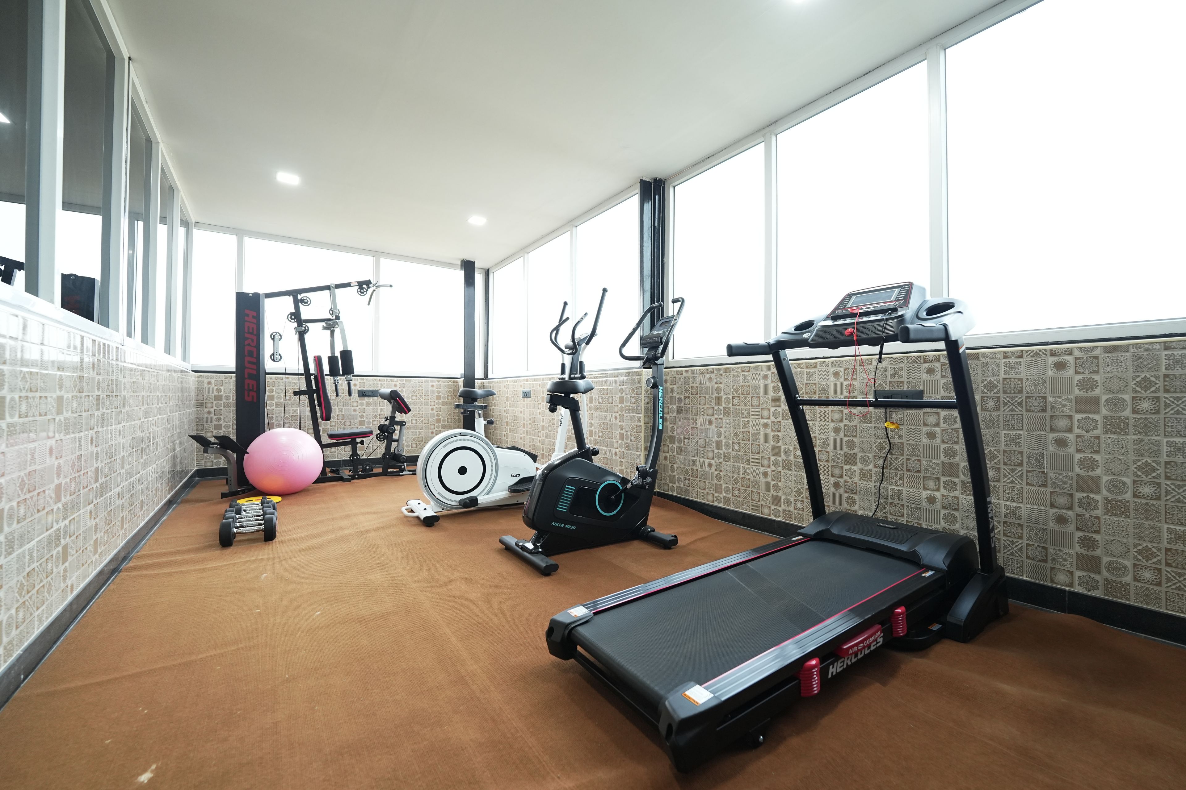 Une salle de sport équipée de divers appareils, notamment un tapis de course, un vélo elliptique et des poids.