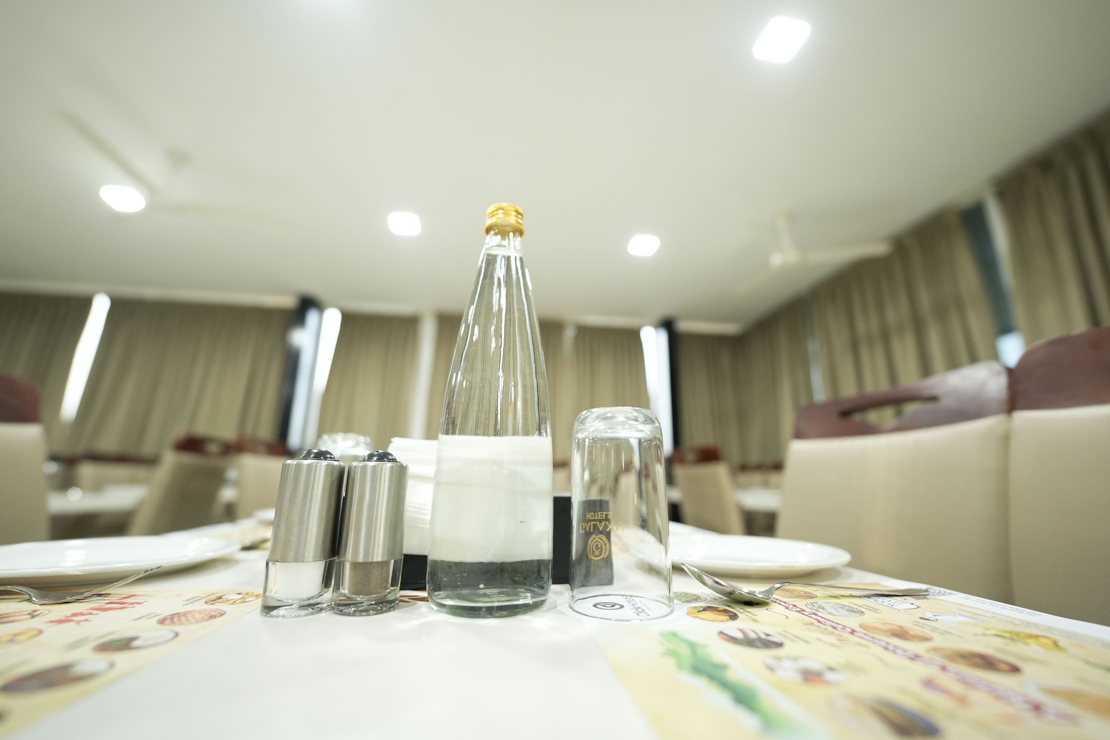 Una mesa de comedor dispuesta con una botella, saleros y pimenteros, una copa y cubiertos.