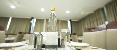 Una mesa de comedor dispuesta con una botella, saleros y pimenteros, una copa y cubiertos.