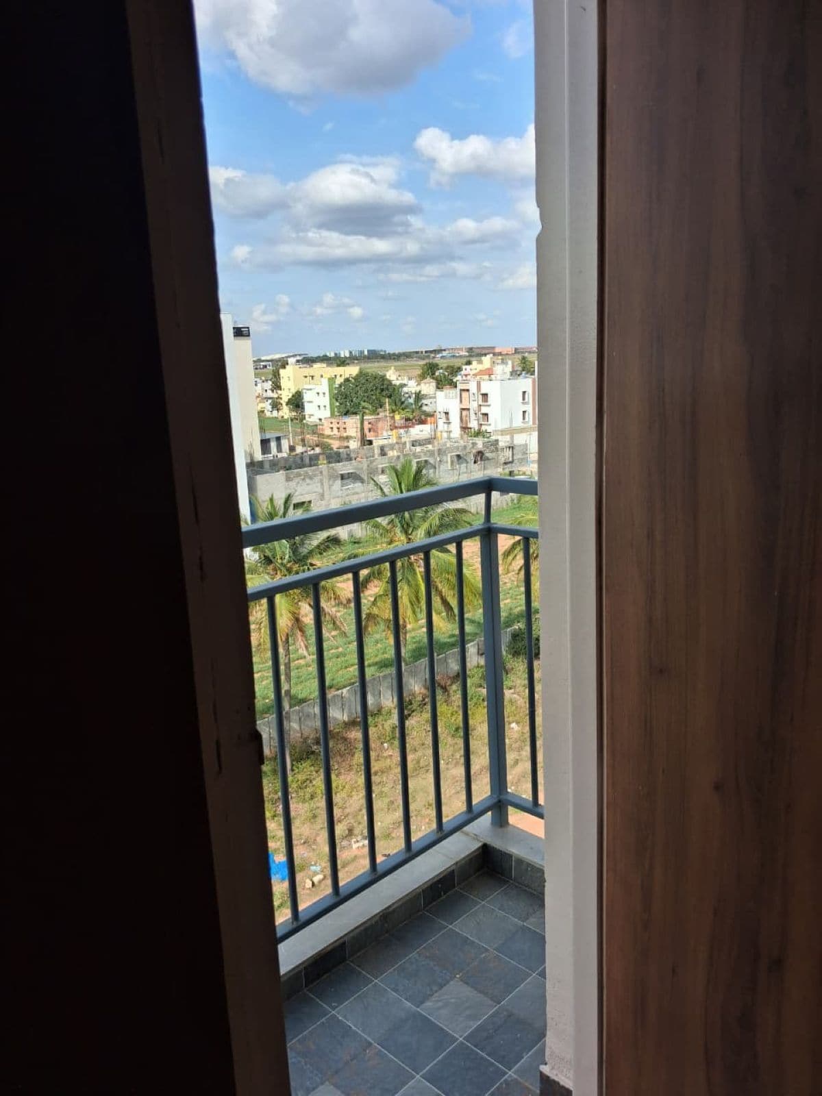A balcony with a metal railing, a tiled floor, and a view of a residential area with buildings and greenery.