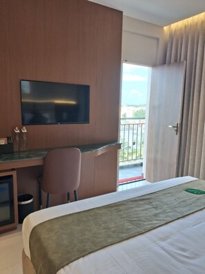 Habitación de hotel con cama, escritorio con silla, televisor y vista al exterior.