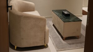Una habitación con un sillón color beige, una mesita con un control remoto y un cuadro en la pared.