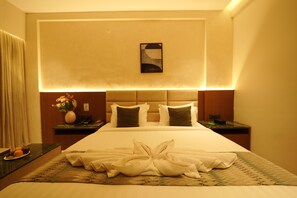 A hotel room with a large bed, a headboard with integrated lighting, a bedside table with a vase of flowers, and a wall-mounted artwork. - Galaxy Air Suites (Bengaluru)