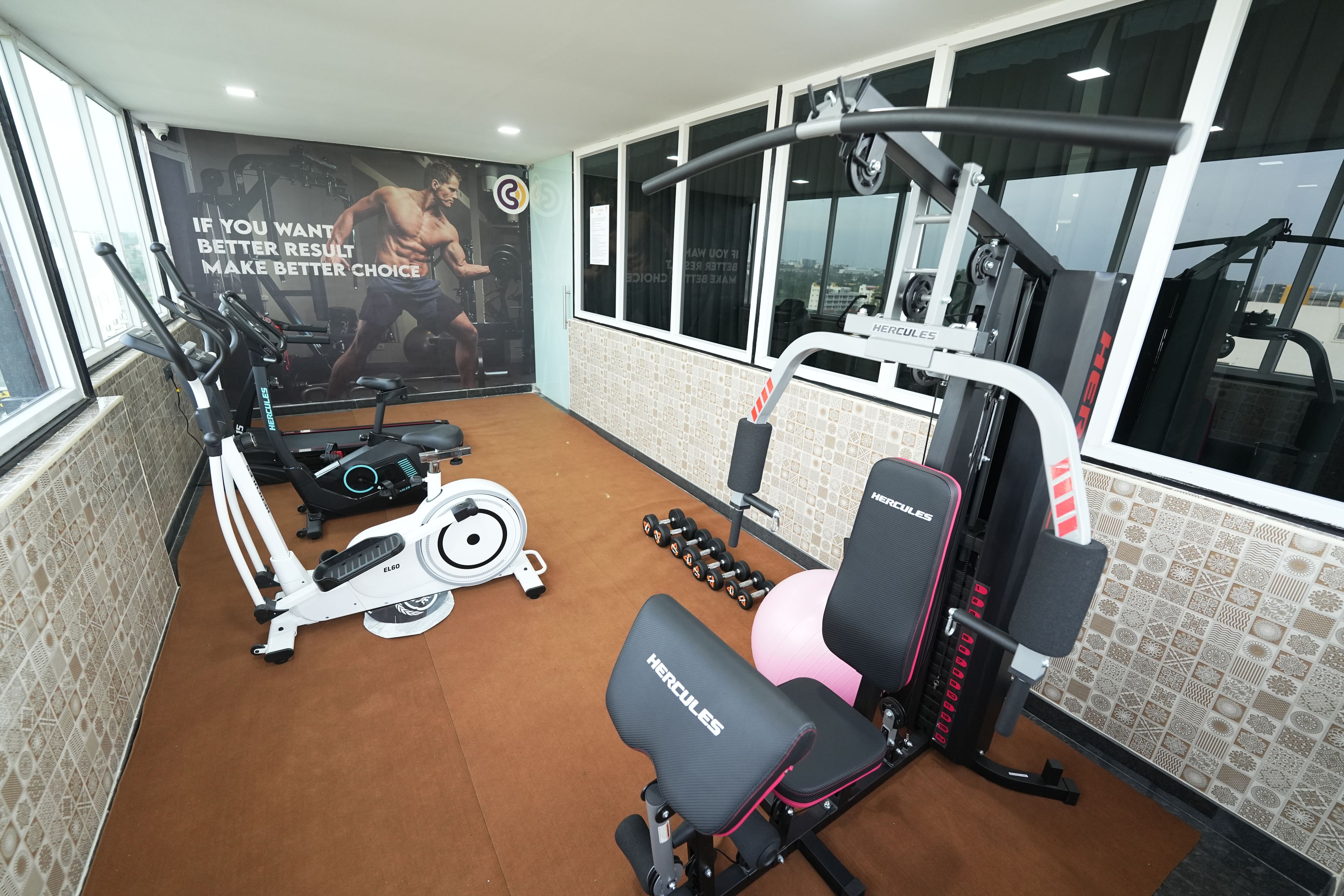 A gym with exercise equipment, a wall with motivational text, and a window with a city view.