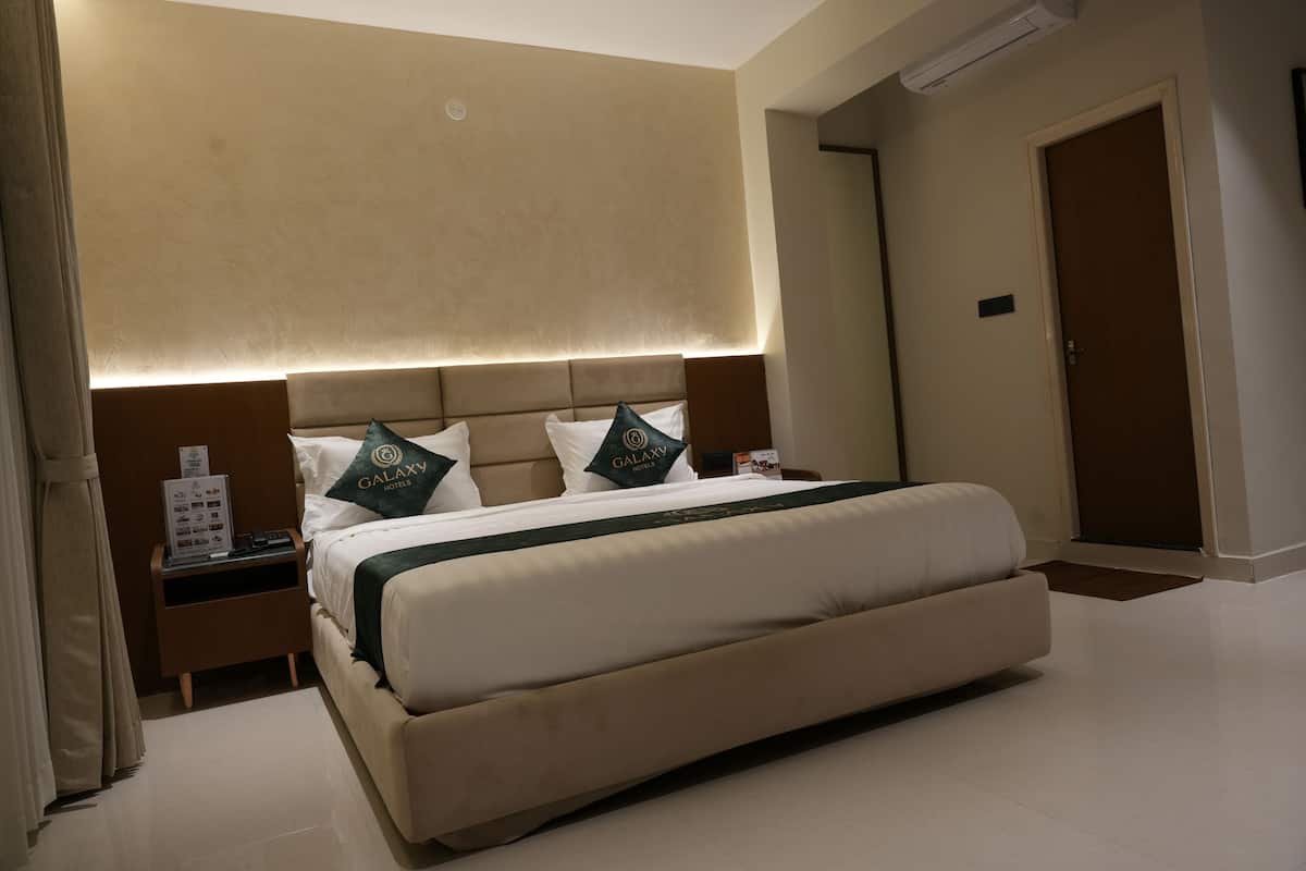 A hotel room with a large bed, a nightstand, a wall-mounted air conditioner, and a door.